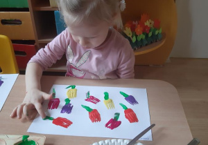 Nikola palcem maluje łodyżki i liście tulipanów.